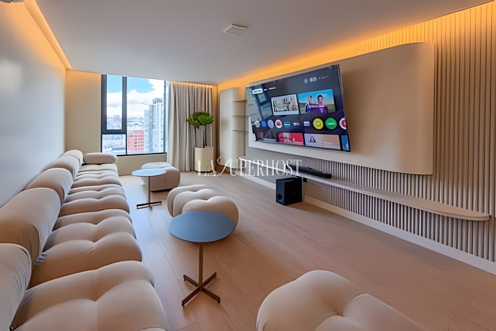 A modern living room with a long sofa, a round coffee table, and a flat-screen TV mounted on the wall.