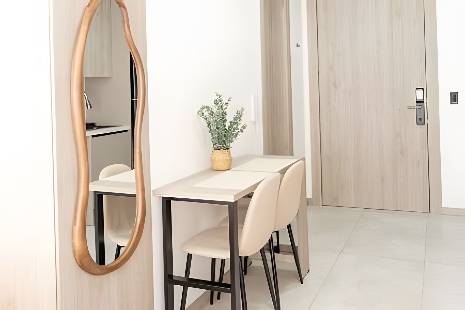 A modern dining area with a round mirror, a potted plant, and a door in the background.