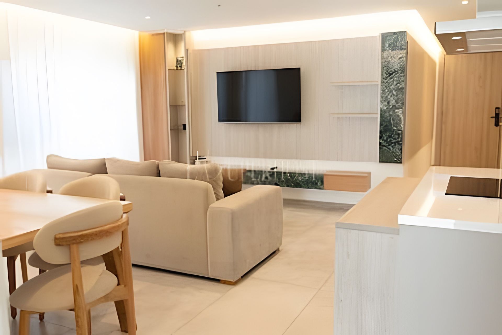 A modern living room with a sofa, a dining table, and chairs. There is a flat-screen TV mounted on the wall.