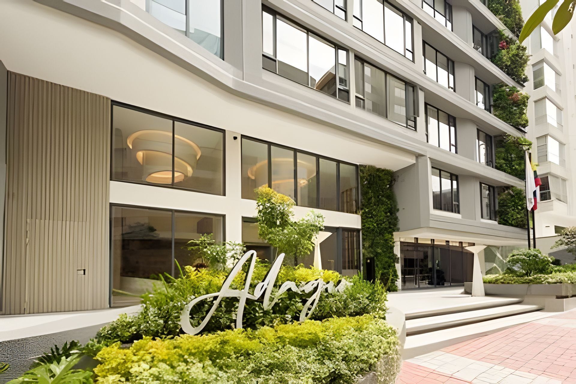 A modern hotel building with large windows, a prominent 'A' sign, and a well-maintained garden area.