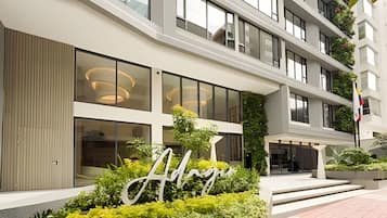 A modern hotel building with large windows, a prominent 'A' sign, and a well-maintained garden area.