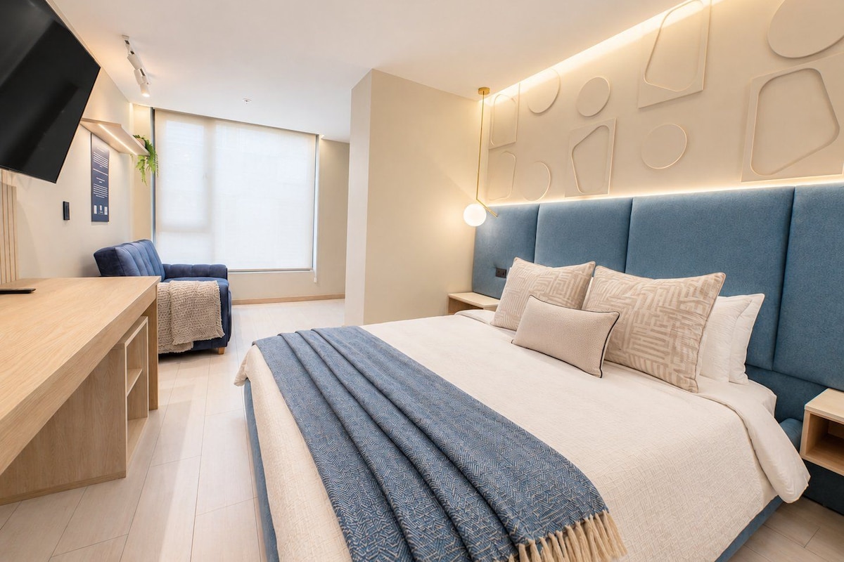 Un dormitorio moderno con una cama grande, mesitas de noche, un escritorio y una televisión.