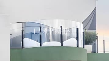 A modern building with a curved glass facade, a green base, and a clear sky in the background.