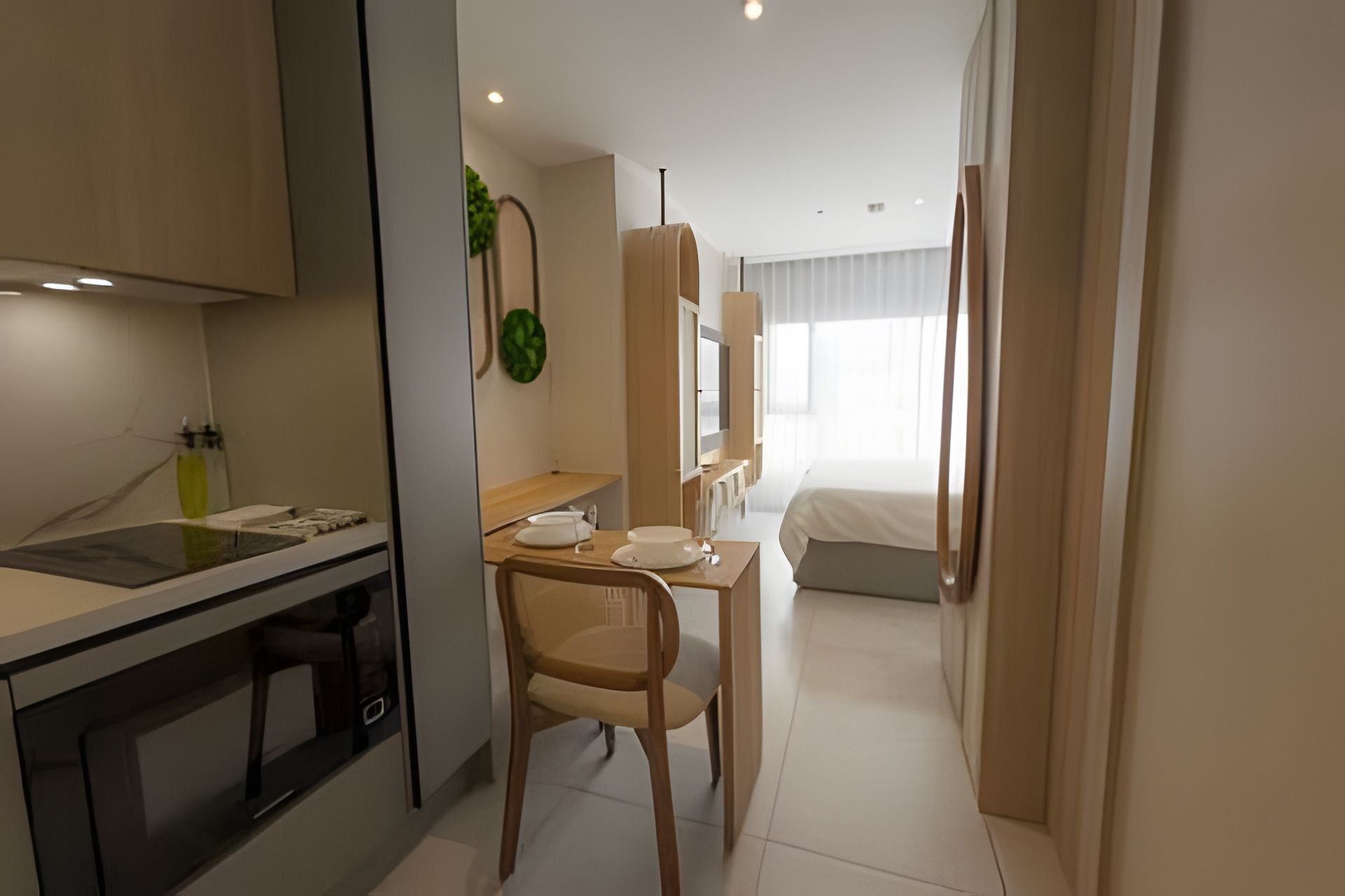 A hotel room with a kitchenette, a dining area with a chair, a bed, and a large window.