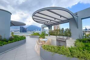 Una terraza panorámica al aire libre con mobiliario y vistas a la ciudad y una montaña.