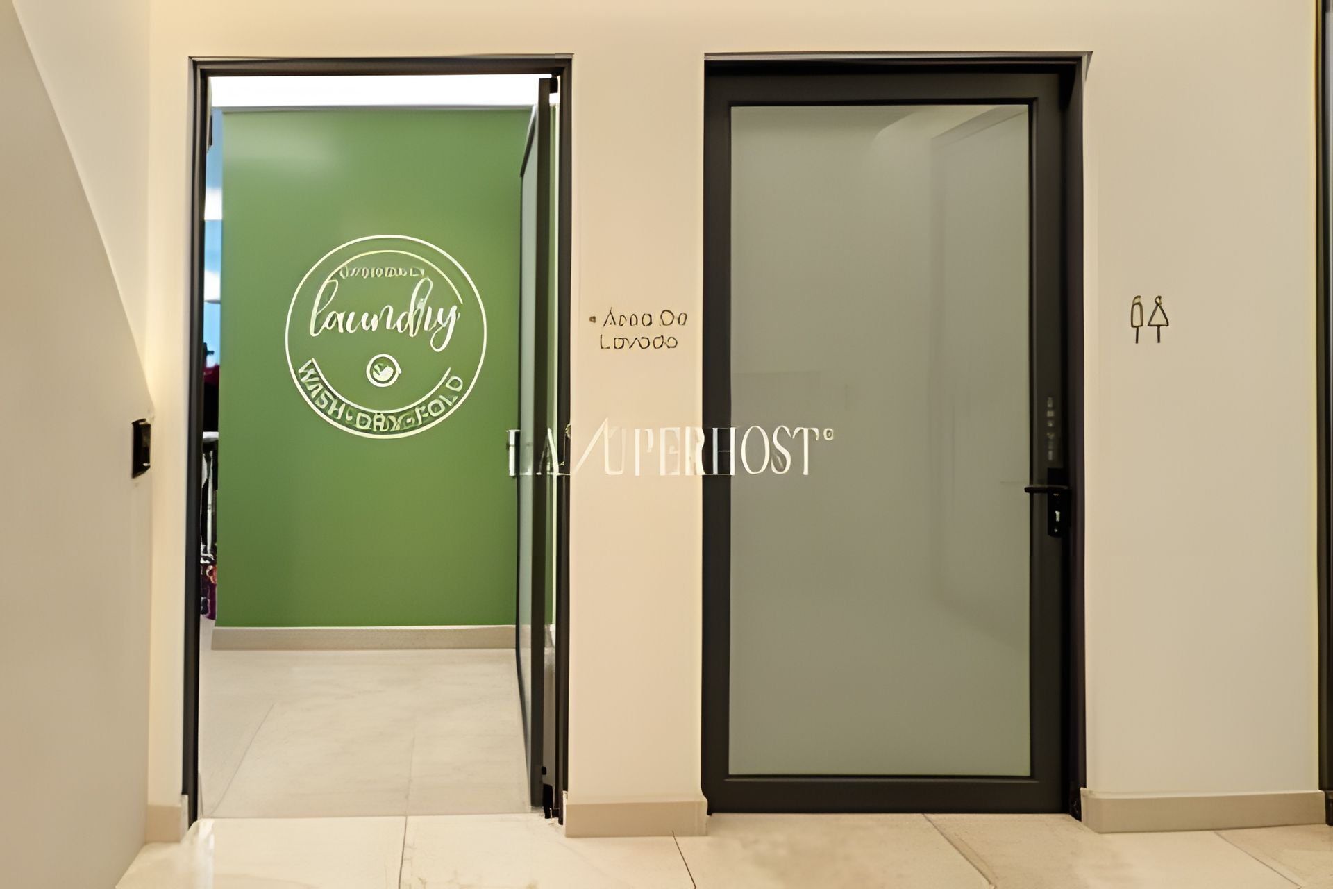 A hallway with a green wall and a door with frosted glass. The green wall has a logo and text indicating a laundry service. The door has a frosted glass panel and a black frame.