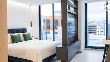 A modern hotel room with a large bed, a flat-screen TV, and a city view.