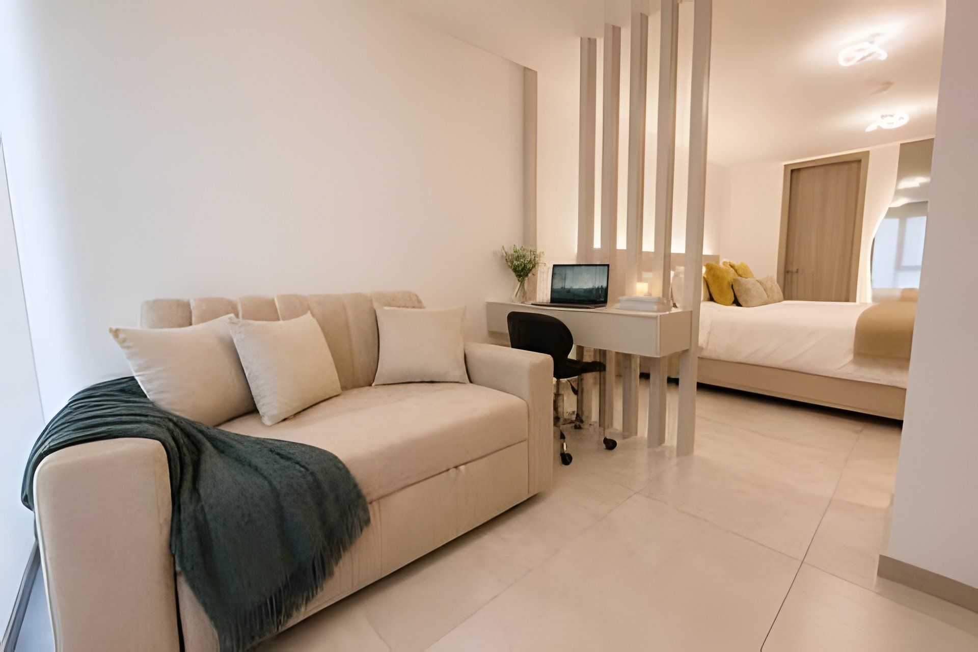 Una sala moderna con sofá, escritorio con laptop y cama con almohadas.