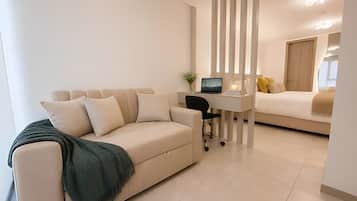 Una sala moderna con sofá, escritorio con laptop y cama con almohadas.