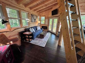 A cozy cabin interior with a sofa, coffee table, and a fireplace. - Treehouse Escape w/Hot Tub, Near Smoky Mtn (Bryson City)