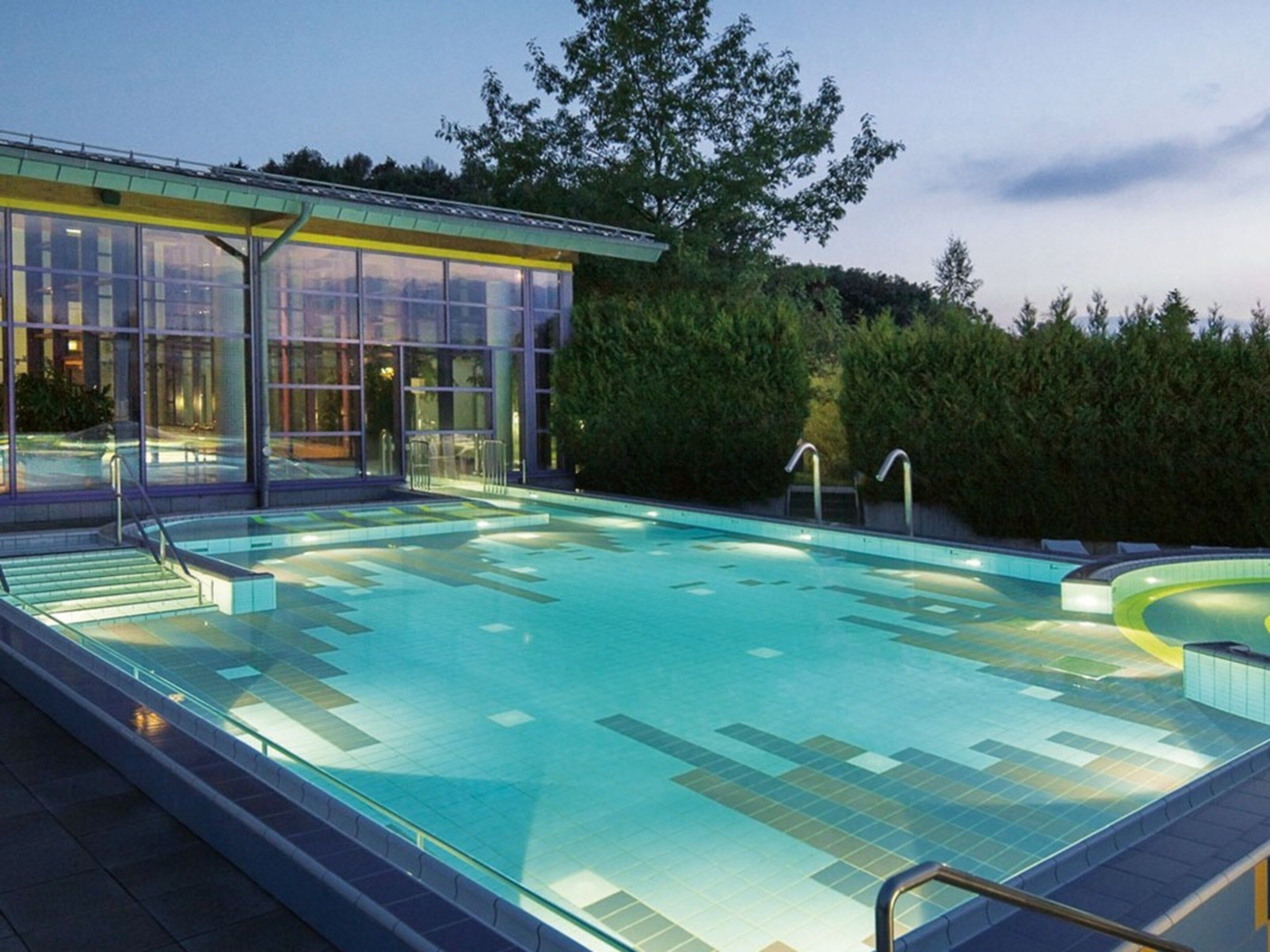 Une piscine dotée d’une enceinte en verre et d’un escalier permettant d’y accéder, le tout entouré de verdure.