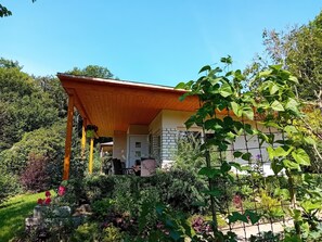 A house with a wooden porch, a brick wall, and a garden with various plants and flowers. - Bungalow Waldidyl im Erzgebirge (Grossolbersdorf)