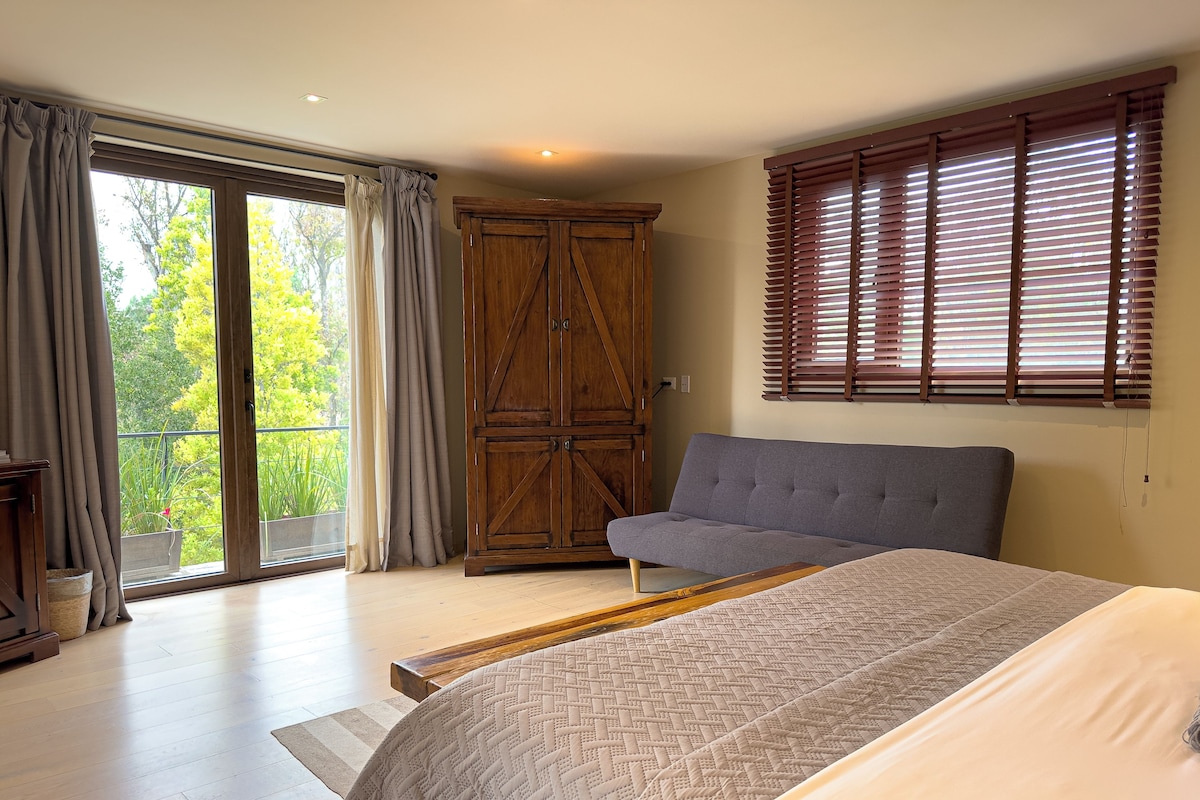 A bedroom with a bed, a sofa, a wooden wardrobe, and a balcony with curtains.