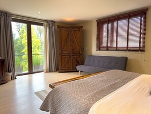 A bedroom with a bed, a sofa, a wooden wardrobe, and a balcony with curtains.