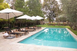 A swimming pool with lounge chairs and umbrellas, surrounded by trees.