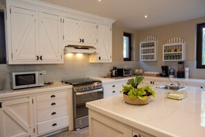 A modern kitchen with white cabinetry, a built-in oven, microwave, and a coffee station.