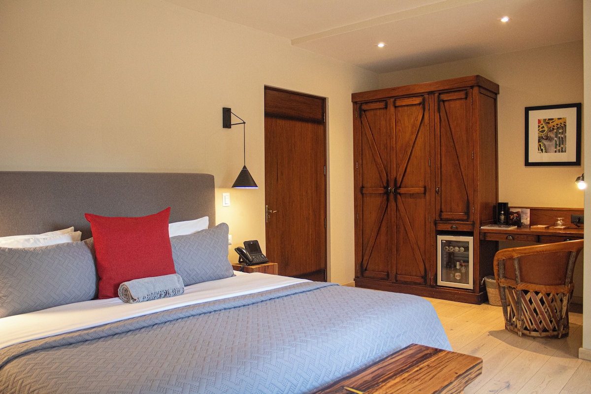 A bedroom with a bed, bedside table, lamp, wardrobe, and a small refrigerator.