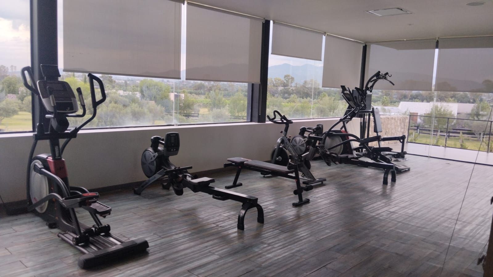 A gym with various exercise equipment, large windows, and a view of greenery.