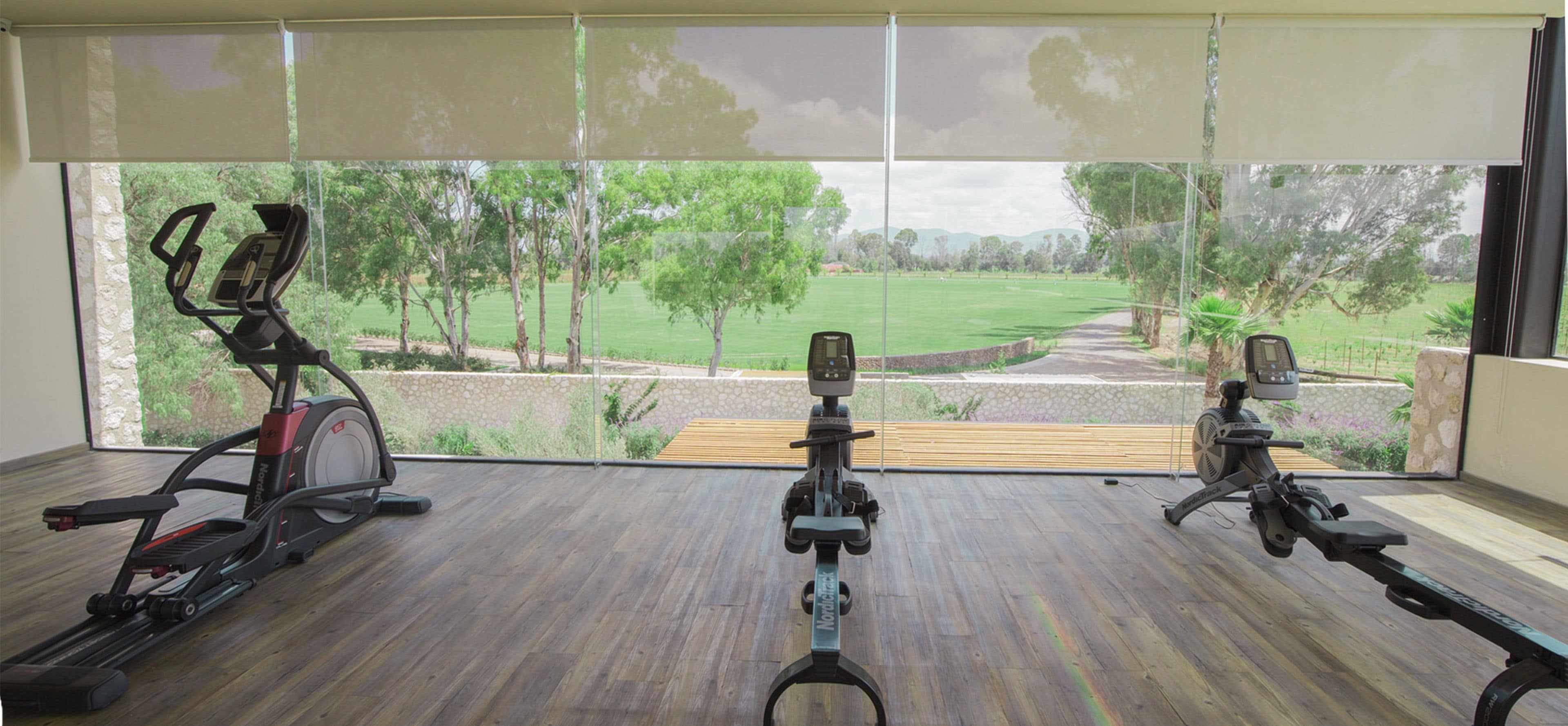 A room with a large window overlooking a green landscape, two stationary bikes, and a wooden bench.