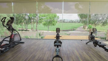A room with a large window overlooking a green landscape, two stationary bikes, and a wooden bench.
