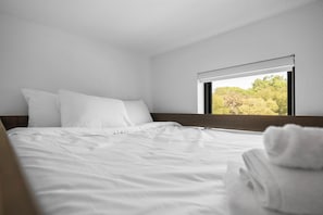 A neatly made bed with white linens and pillows, a window with a view of trees, and a folded towel on the bed. - The Castle Creek Ranch - 5-Acre Ranch, Private Pool, Game Room & Country Getaway (Cross Roads)