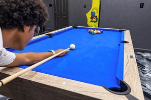 A pool table with a person playing, a yellow wall decoration, and a door in the background. - The Castle Creek Ranch - 5-Acre Ranch, Private Pool, Game Room & Country Getaway (Cross Roads)