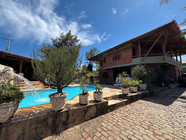 A pool area with a clear blue sky, a brick building with a tiled roof, and potted plants. - 10 minutes from Beach Park - House with sea view 50m from the beach (Aquiraz)