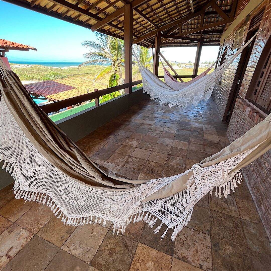 A hammock under a roofed area with a view of the beach.