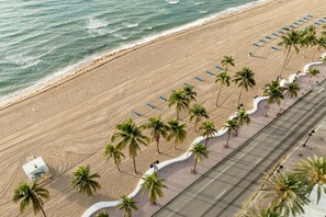 Vue aérienne d’une plage avec une promenade pavée bordée de palmiers et de chaises de plage.