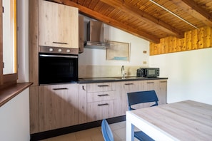 A kitchen with wooden cabinets, a stove, a microwave, and a sink. - Mirafiume - Lugano Lake (San Mamete)