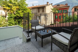 A balcony with wicker furniture, a glass table, and a view of a red building with a tiled roof. - Mirafiume - Lugano Lake (San Mamete)