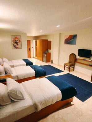 Habitació d'hotel amb tres llits, televisió, escriptori i armari.