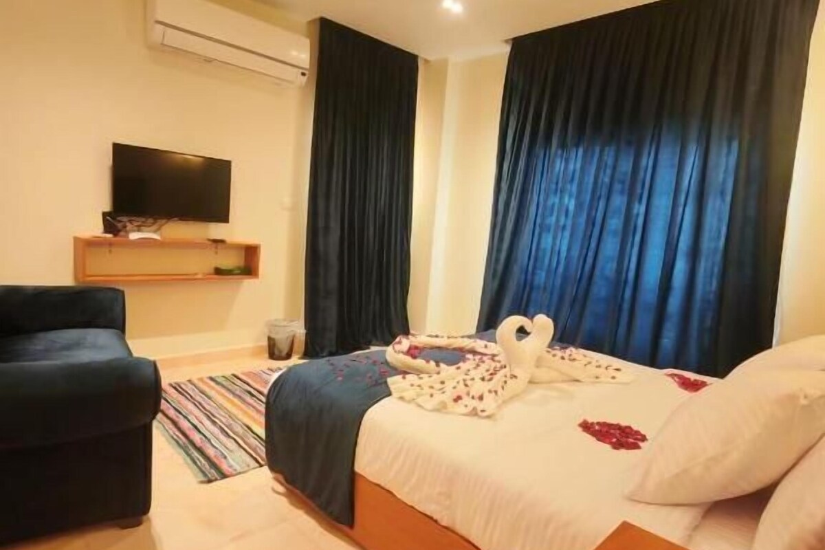 Habitació d'hotel amb llit, cadira, televisió i una taula auxiliar de fusta.