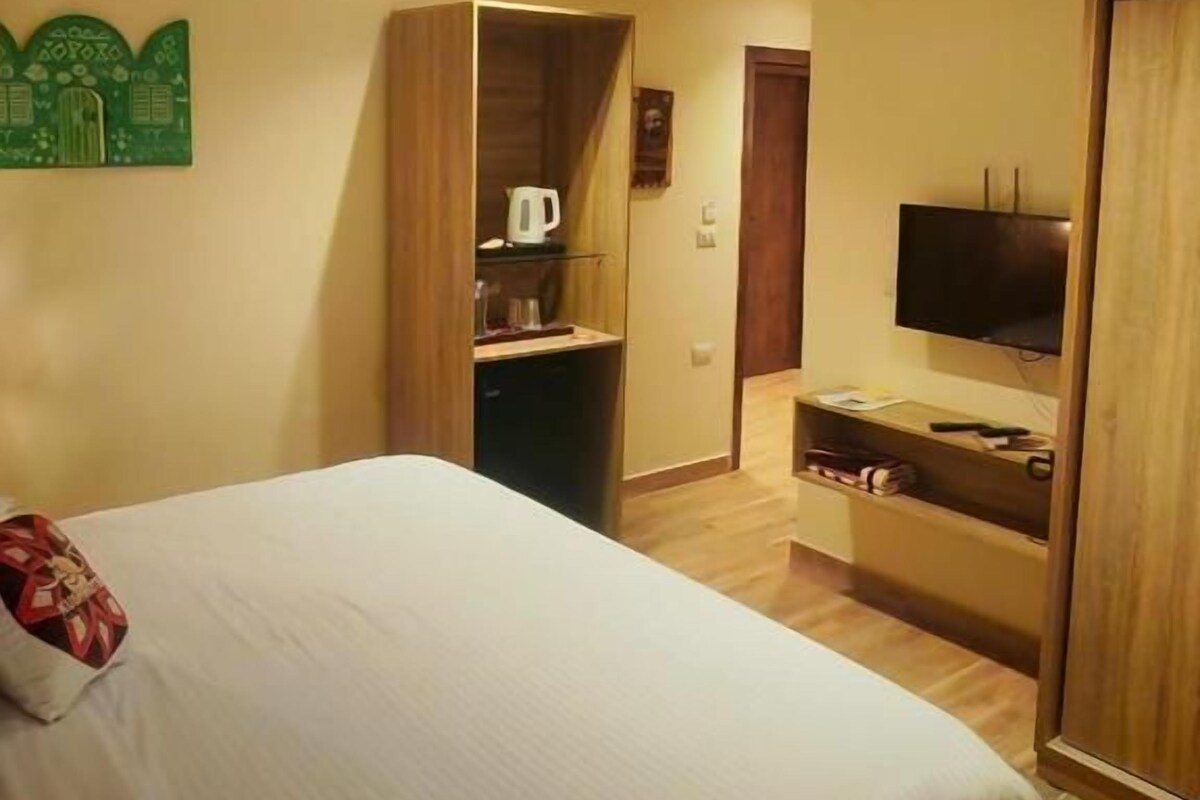 Habitació d'hotel amb llit, armari, televisió i una cuineta petita.
