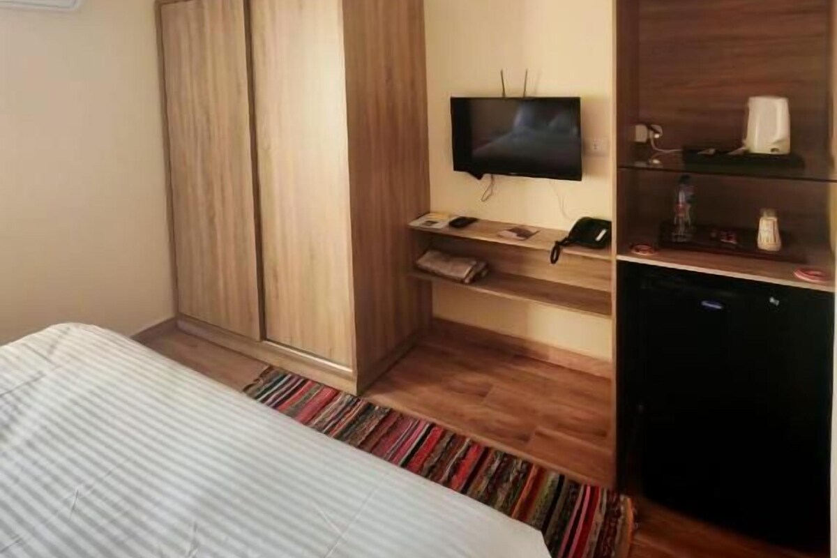 Habitació d'hotel amb llit, armari, televisió i una petita taula amb telèfon i ampolla.