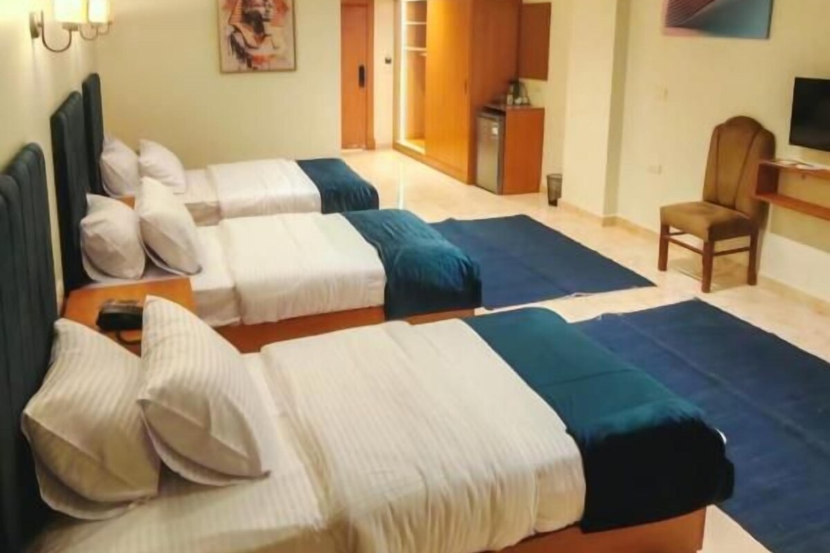 Una habitació d'hotel amb dos llits, una taula de treball, una cadira i un televisor.