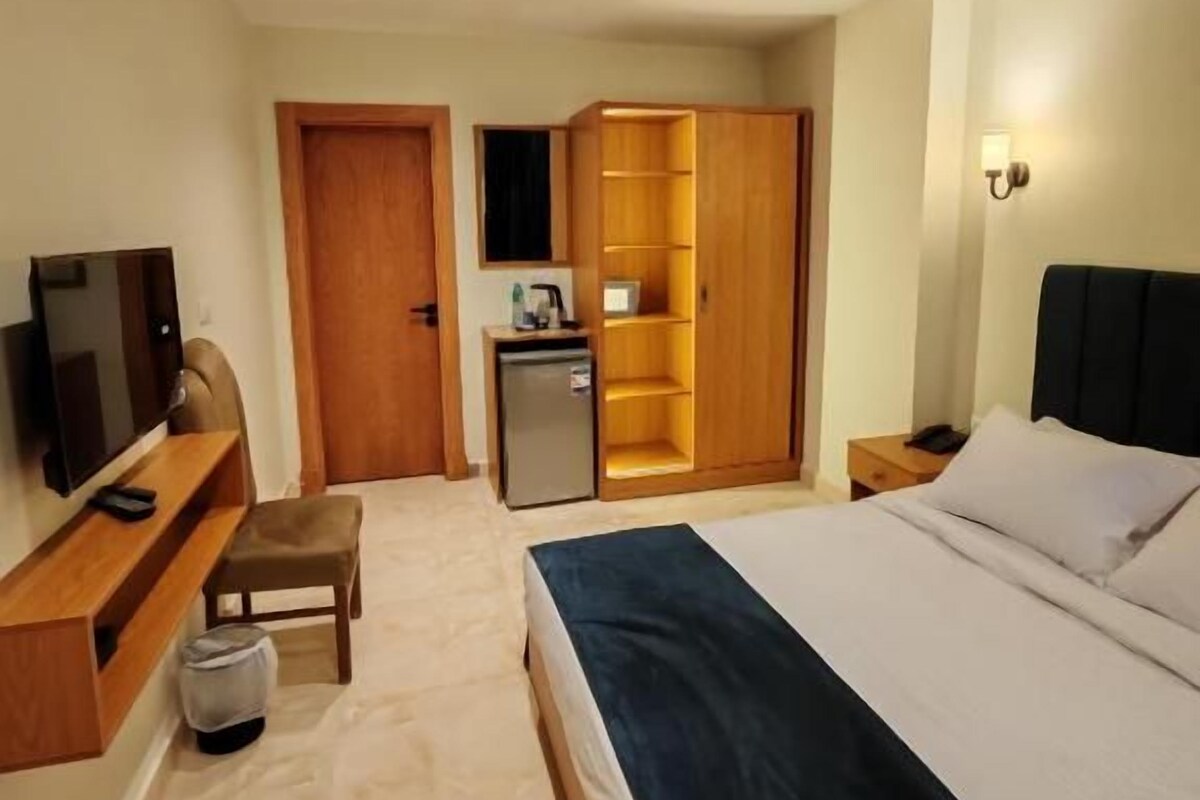 Habitació d'hotel amb llit, televisió, escriptori, armari i petita cuina.