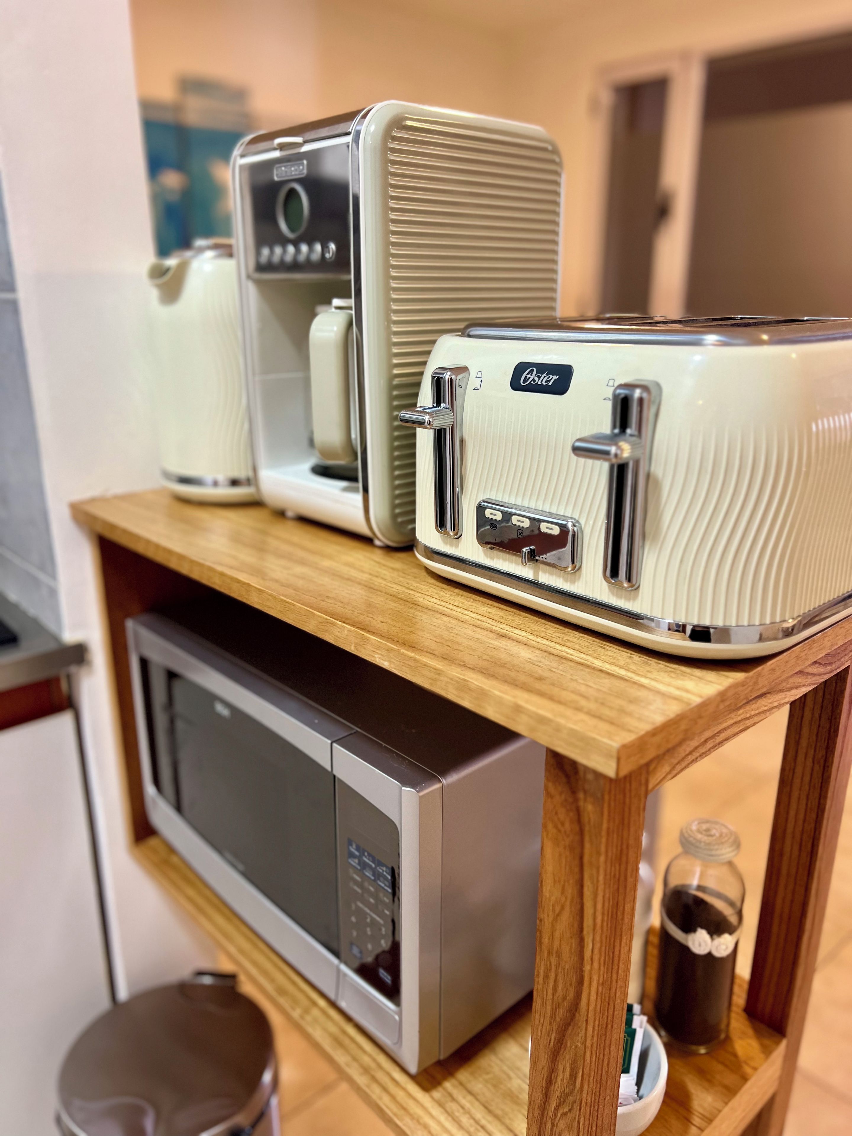 A kitchen with a microwave, toaster, and kettle on a wooden shelf.