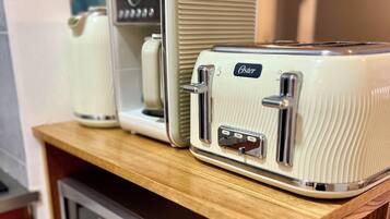 A kitchen with a microwave, toaster, and kettle on a wooden shelf.