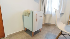 A compact kitchenette with a refrigerator, a chair, and a radiator.