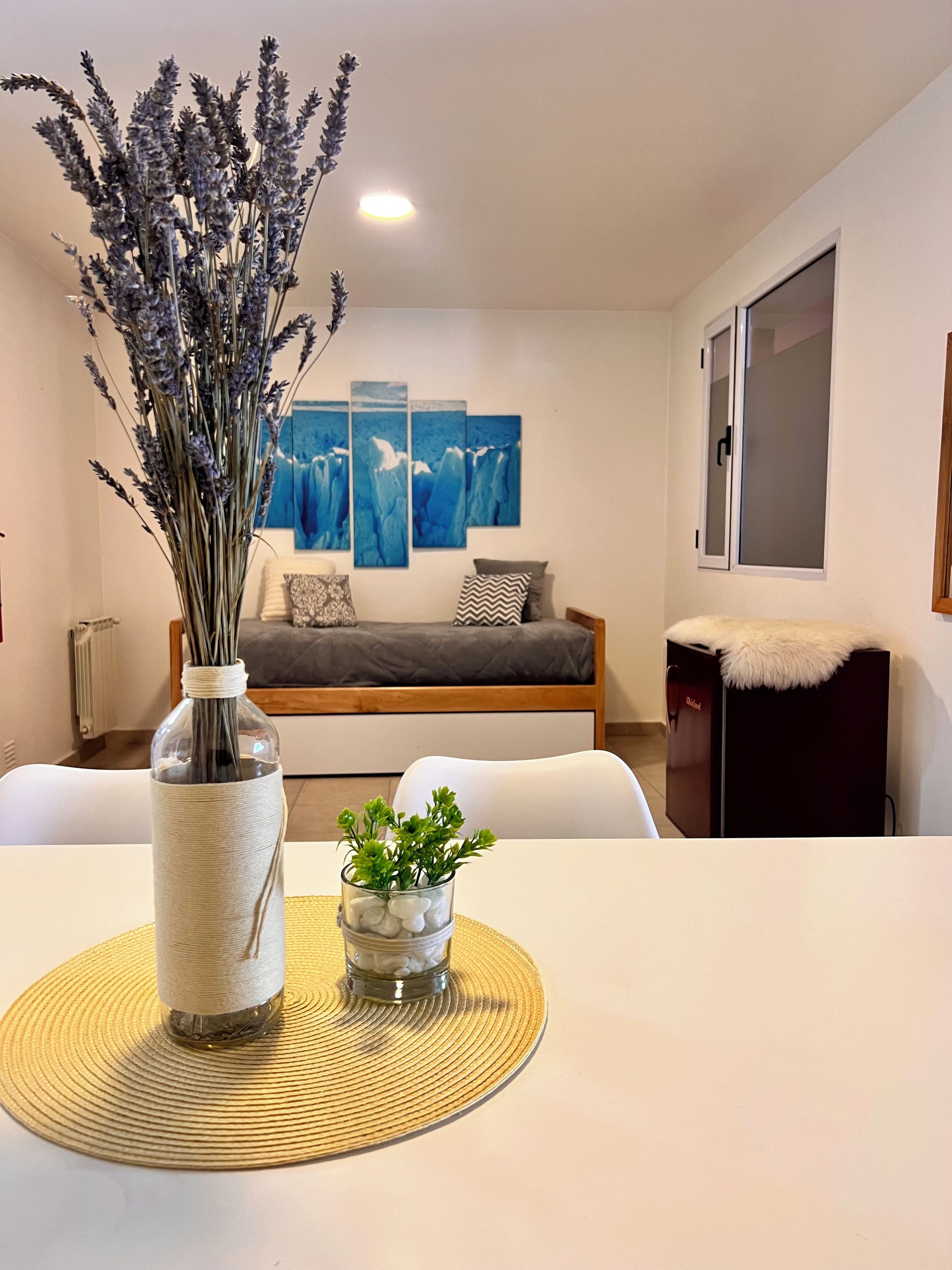 Un salon moderne avec un canapé, une table à manger agrémentée d’un vase et d’une petite plante, et un mur orné de trois tableaux bleus.