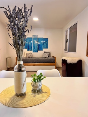 A modern living room with a sofa, a dining table with a vase and a small plant, and a wall with three blue paintings. - Espora (El Calafate)