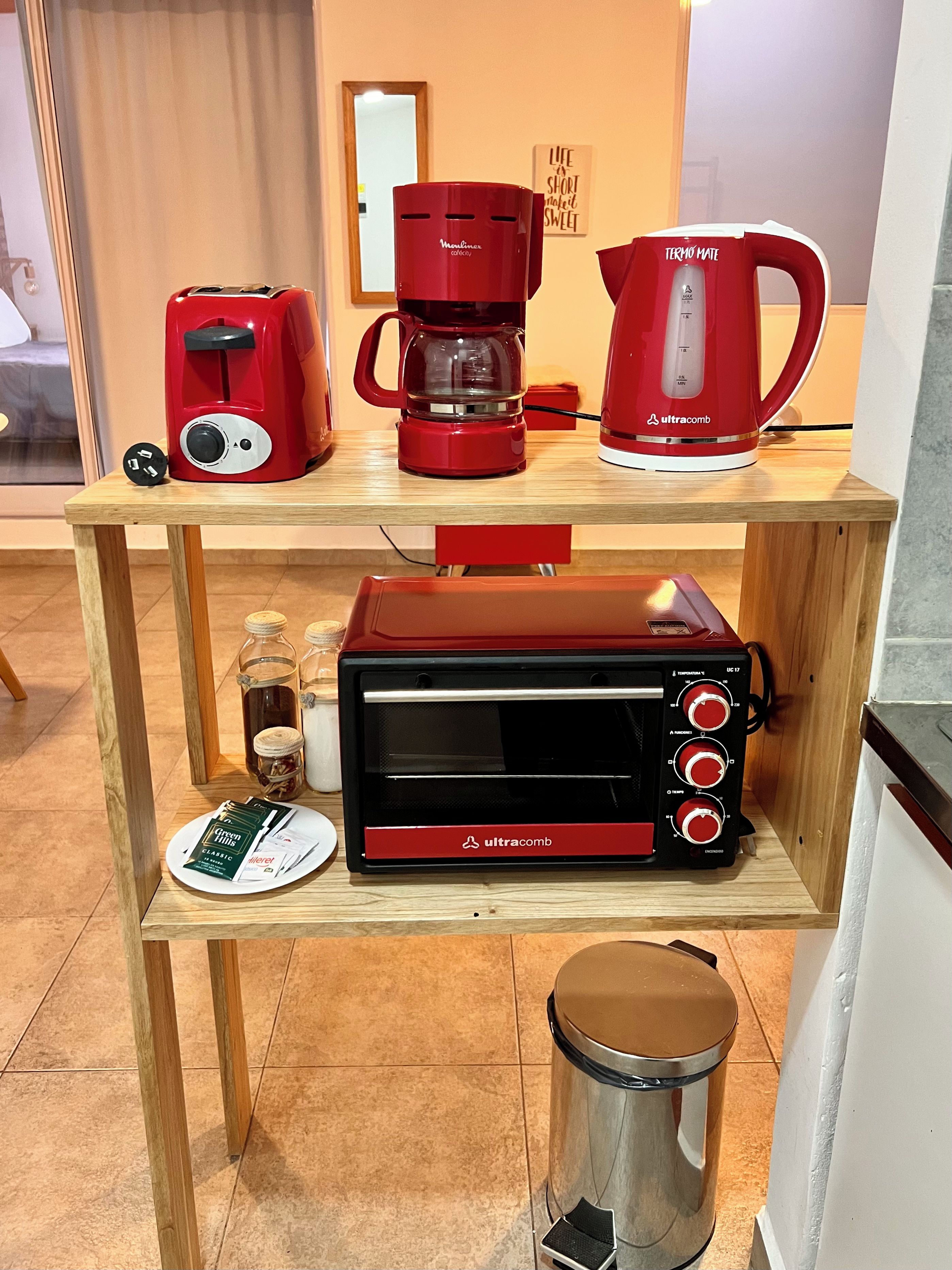 Un coin cuisine comprenant une machine à café, un grille-pain et une tasse rouge posée sur une étagère en bois.