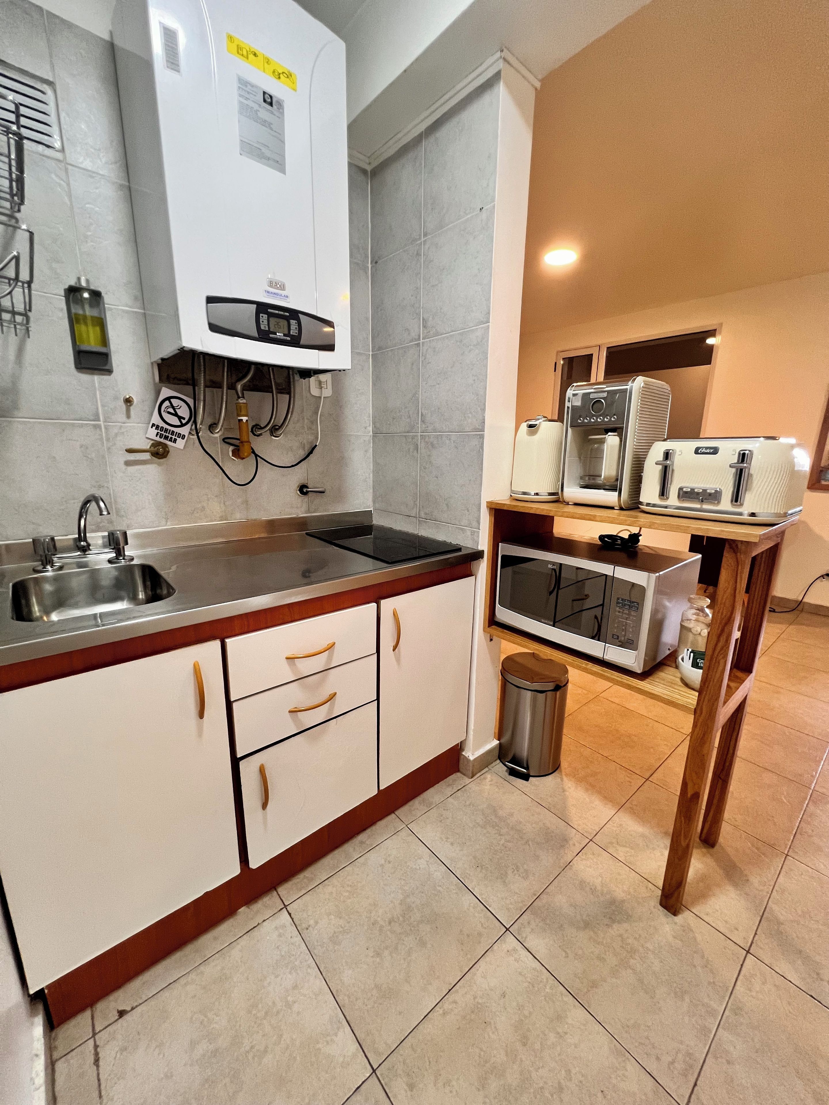 Een compacte keuken met een inbouwoven, magnetron en een koffieapparaat op een houten plank.