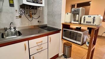 Een compacte keuken met een inbouwoven, magnetron en een koffieapparaat op een houten plank.