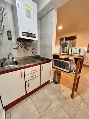 Cozinha compacta com forno embutido, micro-ondas e máquina de café sobre uma prateleira de madeira.