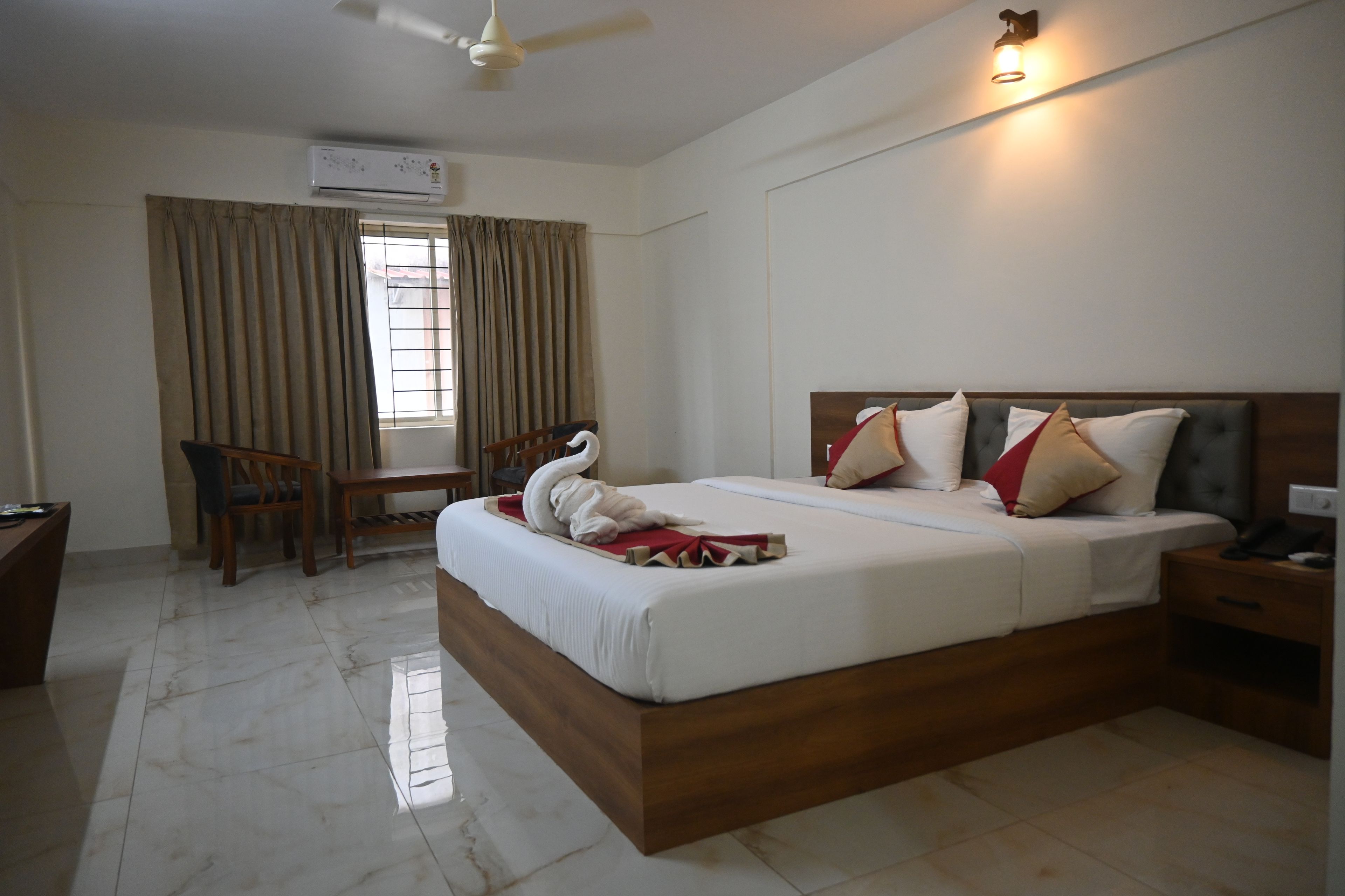 A hotel room with a bed, a desk, a chair, a ceiling fan, and a window with curtains.