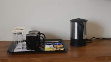 Een dienblad met een koffiezetapparaat, een glazen kan, twee zwarte mokken en zakjes thee op een houten tafel.
