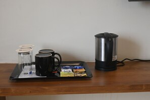 Una bandeja con una cafetera, un recipiente de vidrio para café, dos tazas negras y varios sobres de té sobre una mesa de madera.