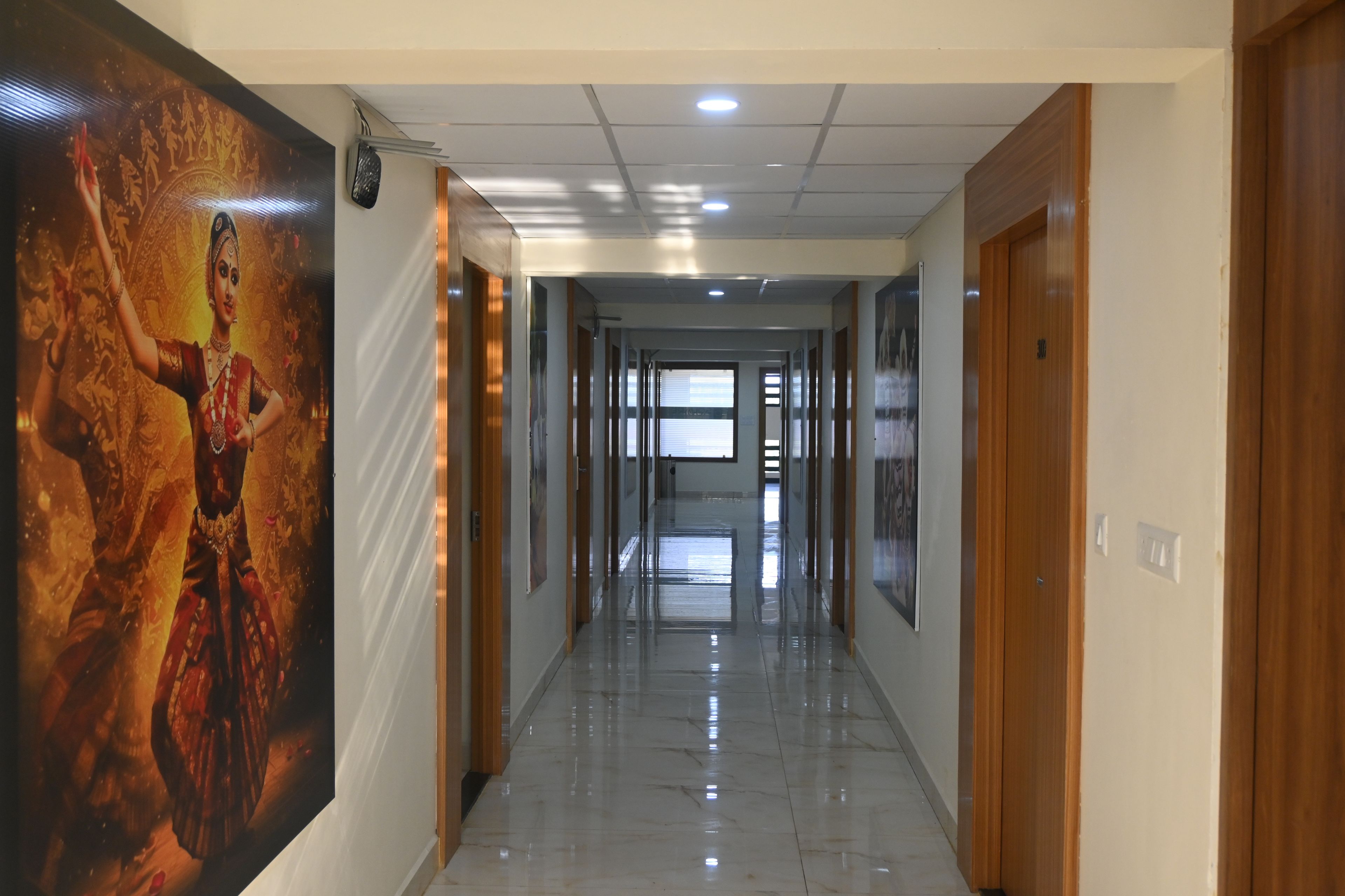 A hotel corridor with a long hallway, wooden doors, and a large poster on the left wall.